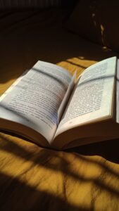 An open book placed on a bed, illuminated by soft sunlight and creating shadows.