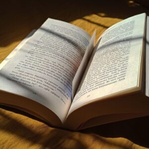 Home An open book placed on a bed, illuminated by soft sunlight and creating shadows.